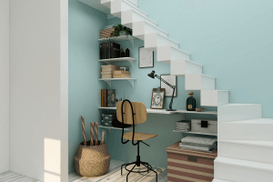 A home office underneath a set of white stairs. 