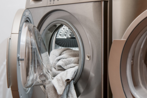 A gray washing machine with the door open and a gray towel hanging out of it.