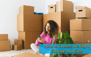 Woman with brown curly hair sitting on floor surrounded by cardboard boxes looking on phone deciding the right storage unit size for her needs.